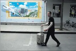  ?? Ng Han Guan ?? The Associated Press A man wheels luggage past a mural depicting air travel and a prosperous city Tuesday in Beijing. The Trump administra­tion will start imposing tariffs Friday on $34 billion in Chinese imports. China plans to counter with its own tariffs.