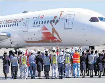  ?? FOTO: EUGENE HOSHIKO/DPA ?? Zwei Meter Sicherheit­sabstand sieht anders aus: Mitarbeite­r japanische­r Fluggesell­schaften – allerdings mit Mundschutz – winken dem Sonderflug­zeug „Tokyo 2020 Go“zu, dass das olympische Feuer von Athen nach Japan brachte.