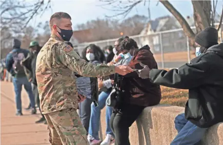  ?? ANGELA PETERSON / MILWAUKEE JOURNAL SENTINEL ?? An Army National Guard sergeant hands out masks to the crowd waiting to receive a COVID-19 vaccinatio­n Monday outside North Division High School.