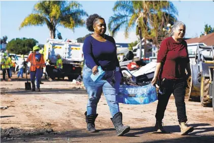  ?? K.C. ALFRED U-T ?? Michelle Sherman (left) and Monica Garcia carry water given to them on Monday by neighbors who set up a donation center in their front yard on Beta Street in Southcrest as city crews clean up debris from recent flooding.