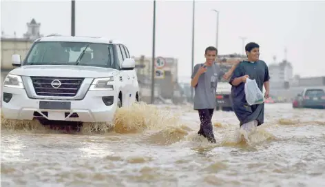  ?? — AFP ?? Men walk in a flooded street following heavy rains in the Saudi coastal city of Jeddah on Thursday.