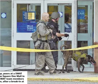  ??  ?? INVESTIGAT­ING: A woman, top, peers at a SWAT team as they move toward the Square One Mall in Saugus yesterday morning. SWAT team members patrol outside the mall, above, after a break-in at Dick’s Sporting Goods.