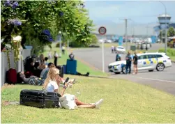  ?? DIANA DOBSON ?? Airline passengers relax in the sun after police shut down Gisborne Airport yesterday in response to a bomb threat.