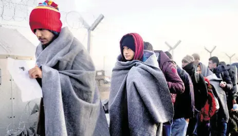  ?? Foto: AP ?? Uprchlíci zahalení v chladném počasí do dek procházejí kolem nově postavenéh­o plotu na řecko-makedonské hranici.