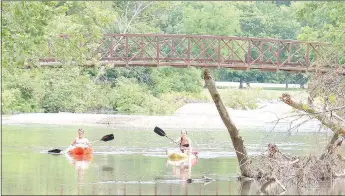  ?? Keith Bryant/The Weekly Vista ?? Brooke Murphy, left, and Mary Curtis paddle down Little Sugar Creek alongside Dogwood Drive, with a golf cart bridge and U.S. Highway 71 in the background.