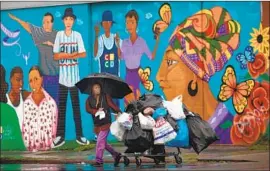  ?? Francine Orr Los Angeles Times ?? EPIFANIA CONDE shields herself from the rain in South L.A. on Wednesday. Some out-of-town visitors found their holiday plans shaken up by the storm.