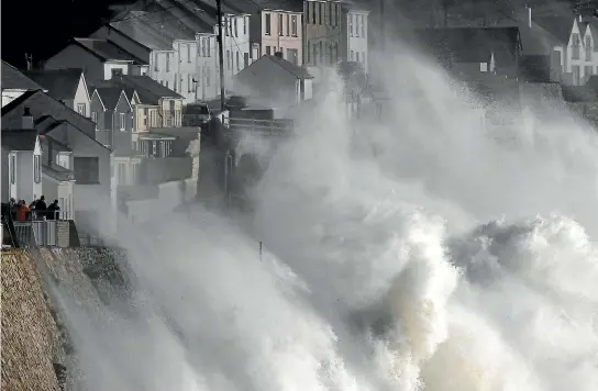  ??  ?? Large waves crash along sea defences and the harbour as storm Ophelia approaches Porthleven in Cornwall, south west Britain. A man photograph­s the sky turning red over buildings in Canary Wharf as dust from the Sahara carried by storm Ophelia filters...