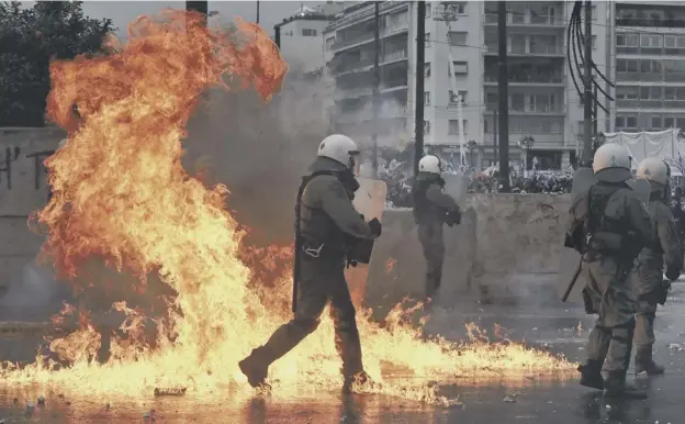  ??  ?? 0 A Molotov cocktail explodes next to Greek riot police during clashes after a rally drew tens of thousands of people to take part in Athens yesterday