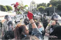  ?? MARIO TAMA GETTY IMAGES ?? A protester holds flowers as police block a street during a demonstrat­ion in the aftermath of George Floyd’s death on Sunday in Santa Monica, Calif.