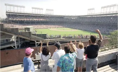  ?? (AP photo/seth Perlman, file) ?? In this Monday, July 9, 1990, file photo, spectators watch an All-star Game practice session from the roof of a building just outside Chicago’s Wrigley Field. Booking hotels for baseball games during shoulder seasons like May, June or September can often be cheaper than the summer months.