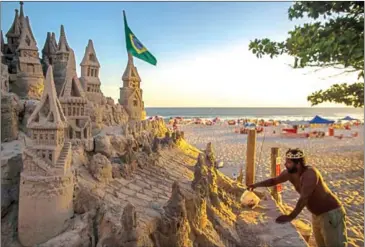  ?? MAURO PIMENTEL/AFP ?? With a crown on his head, Marcio Mizael Matolias, 44, works on his sand castle despite the 40-degree heat that punishes bathers on a sunny summer afternoon on the beach of Barra da Tijuca in Rio de Janeiro, Brazil, on January 18.