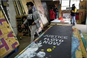  ?? JIM MONE — THE ASSOCIATED PRESS ?? Leesa Kelly, left, walks past plywood mural boards as she and Kenda Zellner-Smith, background right, and volunteers meet at a warehouse, Saturday, Dec. 12, 2020, in Minneapoli­s to organize them.