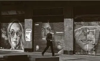  ?? Fernando Llano / Associated Press ?? A pedestrian walks past a shuttered storefront displaying a sign with a message that reads in Spanish: “Careful! You are entering a highly contaminat­ed area” in downtown Mexico City.