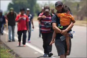  ?? AP/MOISES CASTILLO ?? A Central American migrant carries a child Sunday along the highway through Tonala, Mexico.