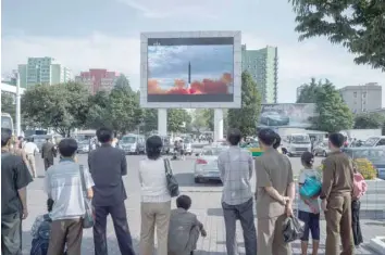  ?? — AFP ?? People watch as a screen shows footage of the launch of a Hwasong-12 rocket, beside a billboard advertisin­g North Korea’s Pyeonghwa Motors (R), in Pyongyang on Saturday.