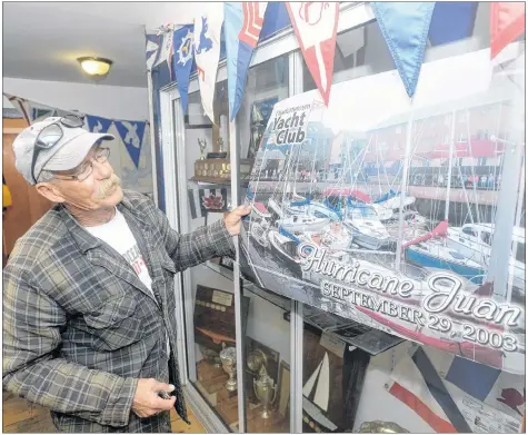  ?? MITCH MACDONALD/THE GUARDIAN ?? Charlottet­own Yacht Club member Doug Gaudet looks over a picture in the club’s display case showing the immediate aftermath of hurricane Juan, which turned the area into a marine graveyard. Gaudet’s boat, the C.C. Comfort (Cheap Canadian Comfort), was among the many destroyed in the storm. He later re-purchased the racing gear on the boat from his insurance company and installed it on his new boat, which he named Spirit of Comfort.