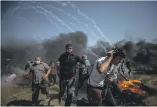  ?? Florian Neuhof for The National; EPA ?? Gazans manoeuvre kites, top, to fly over the border and drop flames on to Israeli farmland, and protesters at the fence run for cover from Israeli tear gas