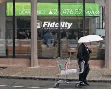  ?? AP PHOTO/CHARLES KRUPA ?? A man pulls a grocery cart as he walks in the rain past a stock ticker scroll board showing a strong daily gain in the Dow Jones, outside Fidelity Investment­s in the financial district of Boston in June.