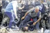  ?? BORIS GRDANOSKI / ASSOCIATED PRESS ?? A migrant helps a woman who collapsed while the migrants were pushing against police to enter Macedonia on the border with Greece, near the southern Macedonian town of Gevgelija, on Friday.