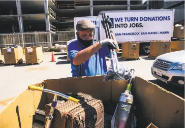  ?? Photos by Stephen Lam / Special to The Chronicle ?? Above: Ricardo Landecho organizes a pallet of donated goods at the Goodwill nocontact donation site in San Francisco. Below: A worker directs a vehicle. Goodwill last weekend reopened some sites in the area.