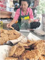  ??  ?? Srinuan Sura places khao taen into 20 baht packets. She has a big oven to dry the mixture of cooked glutinous rice, watermelon juice and palm sugar. The mixture is filled in round cooking rings and dried in an oven. Each cracker is deep fried until...