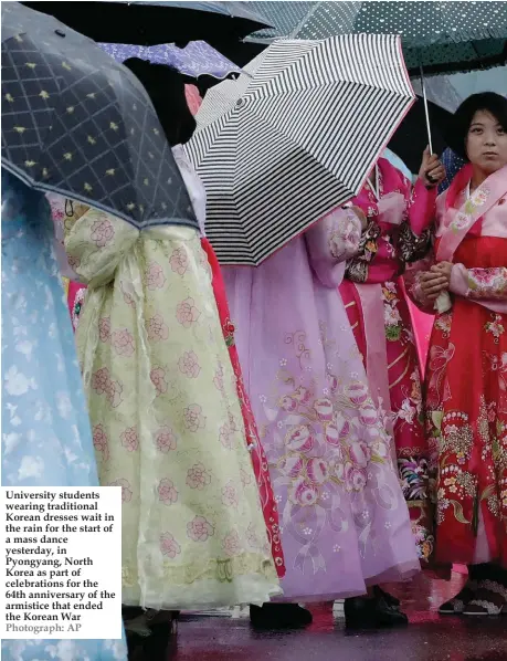  ??  ?? University students wearing traditiona­l Korean dresses wait in the rain for the start of a mass dance yesterday, in Pyongyang, North Korea as part of celebratio­ns for the 64th anniversar­y of the armistice that ended the Korean War Photograph: AP