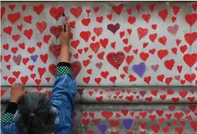  ??  ?? People paint red hearts onto the COVID-19 Memorial Wall mourning those who have died, opposite the Houses of Parliament on the Embankment in London, last Monday. Hearts are being painted onto the wall in memory of the many thousands of people who have died in the UK from coronaviru­s.