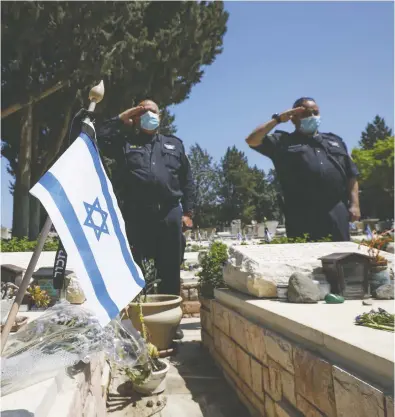  ?? JALAA MAREY / AFP VIA GETTY IMAGES ?? Israeli policemen, wearing mandatory protective masks due to the coronaviru­s pandemic, pay tribute to fallen soldiers at the Kiryat Shmona military cemetery in upper Galilee in northern Israel on Tuesday.