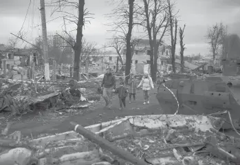  ?? FELIPE DANA/AP ?? A family walks on a road clogged by destroyed Russian tanks last Wednesday in Bucha, Ukraine, near Kyiv.