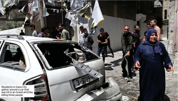  ??  ?? Residents in Gaza City gather around a car that was hit in an Israeli airstrike, killing three people