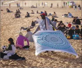  ?? (File Photo/AP/Emilio Morenatti) ?? A street vendor displays sheets for sale Jan. 26 while people sunbathe on the beach in Barcelona, Spain.