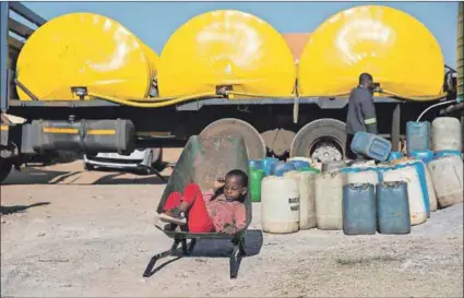  ??  ?? Bypass: Six-year-old Malume Mashilo (above) waits in the wheelbarro­w his siblings will use to transport containers of water from a tank that has just been filled. They live in the Masakhane informal settlement, which borders the Duvha power station and an open-cast coal mine.