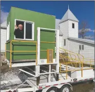  ?? (Minot Daily News) ?? Pastor Jonathan Starks of Calvary Church in Ryder, N.D., waves from a deer stand parked on a trailer. The deer stand, provided by a local resident, offers protection for holding the drive-in worship services. The church, in the background, doesn’t have room for social distancing.