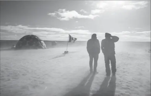  ??  ?? Parks Canada ’s Marc-Andre Bernier and Thierry Boyer turn their backs to blowing sand as a plane takes off from Davit camp on Saunitalik Island, Nunavut .