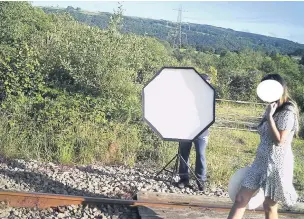  ??  ?? A photograph­y lighting umbrella is held in position as a woman poses for photos on the train track in Cilfrew.