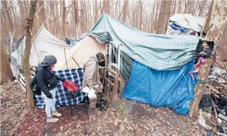  ?? JOHN MUNSON/AP ?? Jose Ortiz unlocks the gate to the residence he built in the homeless encampment known as the Jungle earlier this month in Ithaca, New York. Tas’a Towsley, a friend, is with him. With the pandemic raging and winter here, communitie­s are getting creative in helping the homeless.