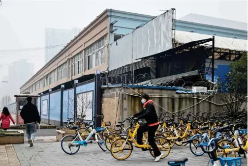  ?? Agence France-presse ?? People walk past the closed Huanan Seafood wholesale market in Wuhan, China’s central Hubei province on Saturday.
