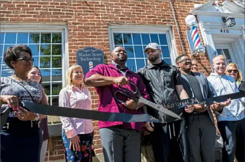  ?? Michael M. Santiago/Post-Gazette photos ?? Darnell Samuel, owner of Market Street Barbershop, center, is surrounded by employees and friends as he cuts a ribbon during a ceremony sponsored by the Fayette County Chamber of Commerce at Market Street Barbershop in Brownsvill­e.