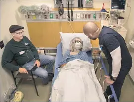  ?? Gina Ferazzi Los Angeles Times ?? NURSE Reggie Withers, right, tends to f lu patient Louise Dominguez in the emergency room at Torrance Medical Center as her son Al watches.