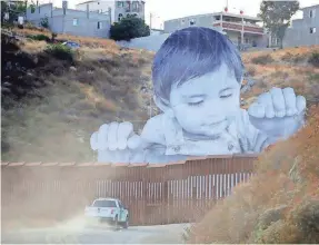  ?? GREGORY BULL/AP ?? A U.S. Border Patrol vehicle drives in front of art in Tecate, Mexico, just beyond the border fence. A French artist known as JR hopes the display will prompt a discussion about immigratio­n.