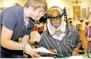  ?? Diana L. Porter / For the Chronicle ?? Matthew Tomlin, 17, presents Legend Oaks resident John Elloie with a custom adoption certificat­e at the Adopt-a-Pop luncheon/ice cream social at Legend Oaks Healthcare and Rehabilita­tion in Katy on June 19.