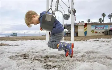  ?? JAY L. CLENDENIN Los Angeles Times ?? THIS BEACH BLANKET in Manhattan Beach on Friday morning was left by a hailstorm. Graham Johnson, 3, looks at grains of sand and ice from a swing. Some Southland beaches were later closed because of lightning.