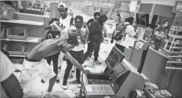  ?? RICHARD TSONG-TAATARII/STAR TRIBUNE ?? A looter uses a claw hammer as he tries to break into a cash register at a Target store in Minneapoli­s on Wednesday.