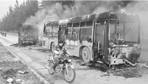  ??  ?? A man on a motorcycle drives past burning buses while en route to evacuate ill and injured people from the besieged Syrian villages of al-Foua and Kefraya, after they were attacked and burned, in Idlib province, Syria. — Reuters photo