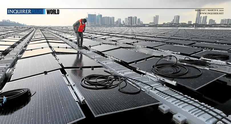  ?? —PHOTOS BY AFP ?? MAKING WAVES A worker checks cables on a floating solar power farm off Singapore’s northern coast just across the Malaysian state of Johor (background). With little space on land, Singapore has put thousands of solar panels on water.