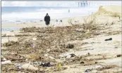  ?? PHOTO VIA AP ?? A man, dog and two kids walk near a pile of trash and debris on the beach that washed down the Santa Ana River in Huntington Beach on Monday after the recent rain storms that hit Southern California.