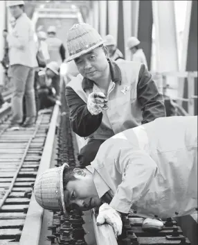  ?? DONG WEIGUO / FOR CHINA DAILY ?? Zhang Xinchao (top), 50, checks the rails with colleagues on a section of the Xinxiang bridge.