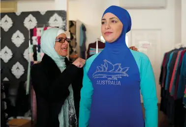  ?? (Jason Reed/Reuters) ?? AHEDA ZANETTI adjusts one of the burkini swimsuits she designed on a model at her fashion store in Sydney.