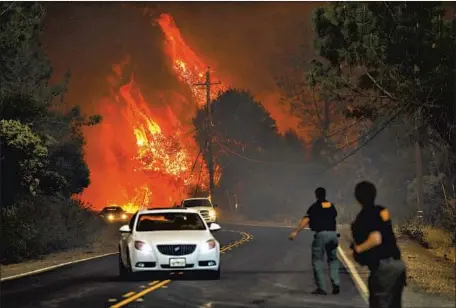  ?? GABRIELLE LURIE San Francisco Chronicle ?? SHERIFF’S DEPUTIES yell to drivers to evacuate the area off Pentz Road as the Camp fire rages in Paradise, Calif., in November 2018.