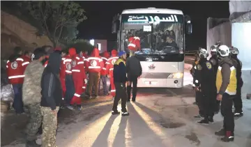  ??  ?? Syrian rebel fighters, members of the Syrian Red Crescent, and Civil Defence stand around a bus that is part of a convoy carrying rebel fighters and civilians as it arrives in the town of Qalaat al-Madiq after their evacuation from the Eastern Ghouta...